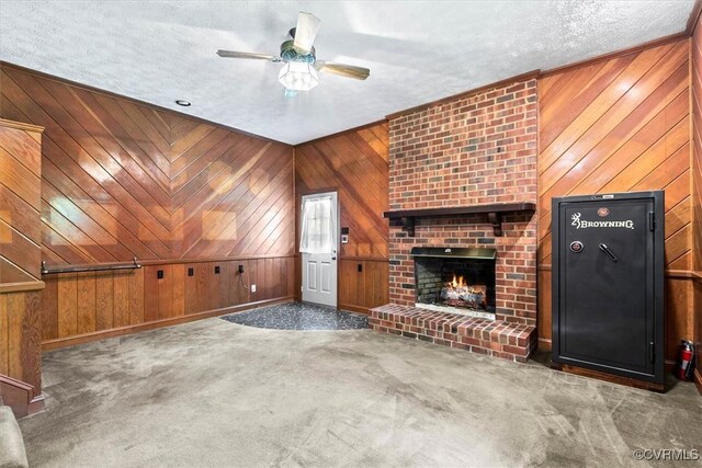 unfurnished living room featuring a fireplace, carpet flooring, wood walls, ceiling fan, and a textured ceiling