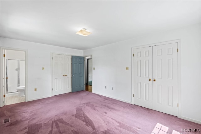 unfurnished bedroom featuring ensuite bath, light carpet, and two closets