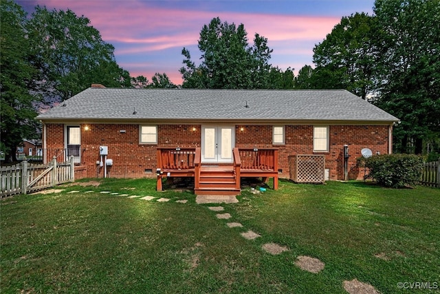 back house at dusk featuring a lawn and a deck