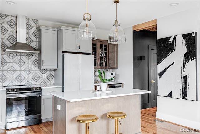 kitchen with white refrigerator, a kitchen island, stainless steel electric stove, and wall chimney exhaust hood