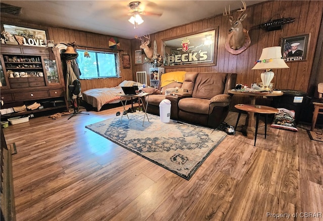 living room with wood-type flooring, ceiling fan, and wooden walls