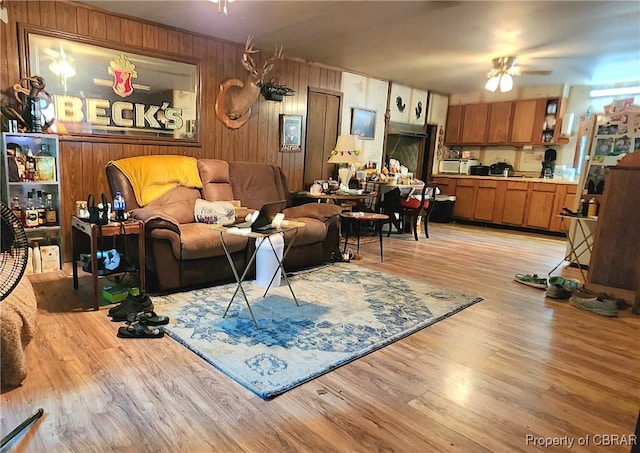 living room with light wood-type flooring, ceiling fan, and wooden walls