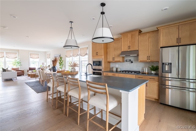 kitchen with light wood-type flooring, a kitchen island with sink, decorative backsplash, a breakfast bar, and appliances with stainless steel finishes