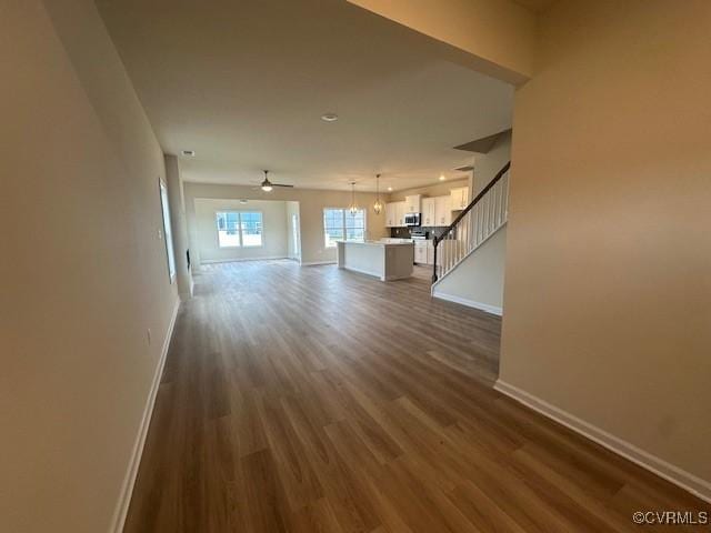 unfurnished living room featuring dark wood-type flooring and ceiling fan