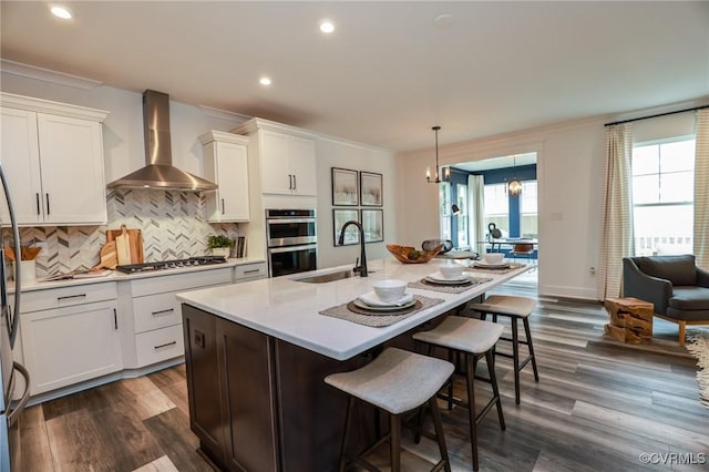 kitchen with a sink, stainless steel appliances, crown molding, and wall chimney range hood