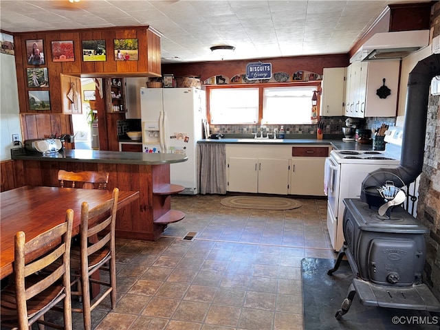 kitchen featuring white appliances, a wood stove, kitchen peninsula, sink, and white cabinetry