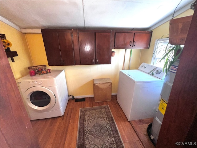 clothes washing area with wood-type flooring, washer and dryer, cabinets, and electric water heater