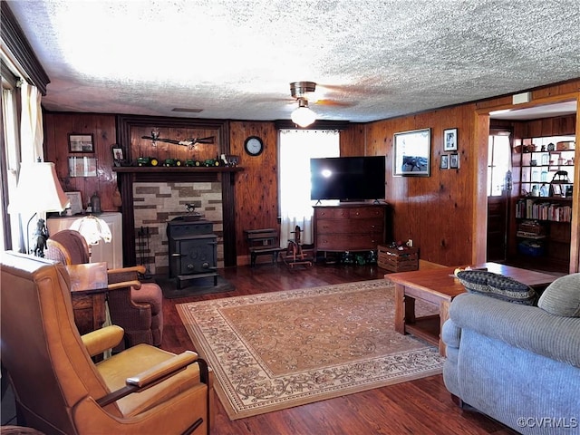 living room with wood walls, a wood stove, a textured ceiling, a ceiling fan, and wood finished floors