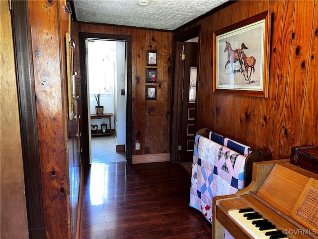 hall featuring dark wood-type flooring, baseboards, a textured ceiling, and wood walls