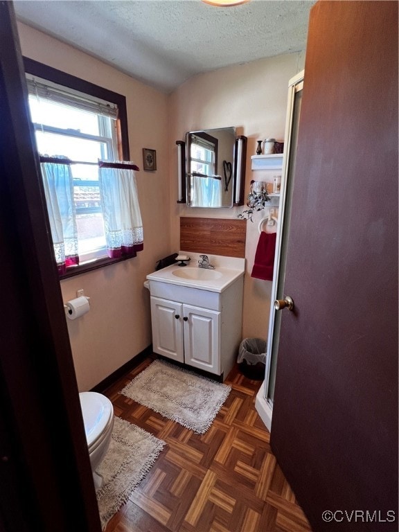 bathroom with an enclosed shower, toilet, vanity, parquet floors, and a textured ceiling