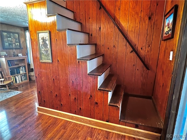 stairs with a textured ceiling, wood-type flooring, and wooden walls