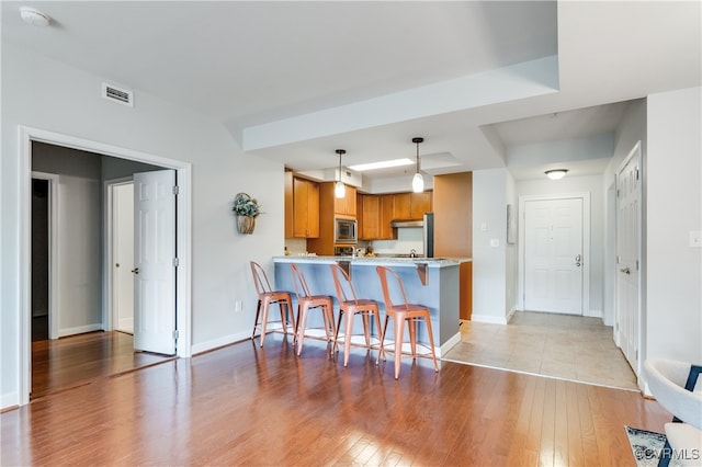 kitchen featuring kitchen peninsula, decorative light fixtures, light hardwood / wood-style flooring, a breakfast bar, and stainless steel microwave