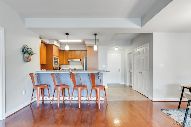 kitchen with stainless steel microwave, kitchen peninsula, a breakfast bar area, light wood-type flooring, and decorative light fixtures