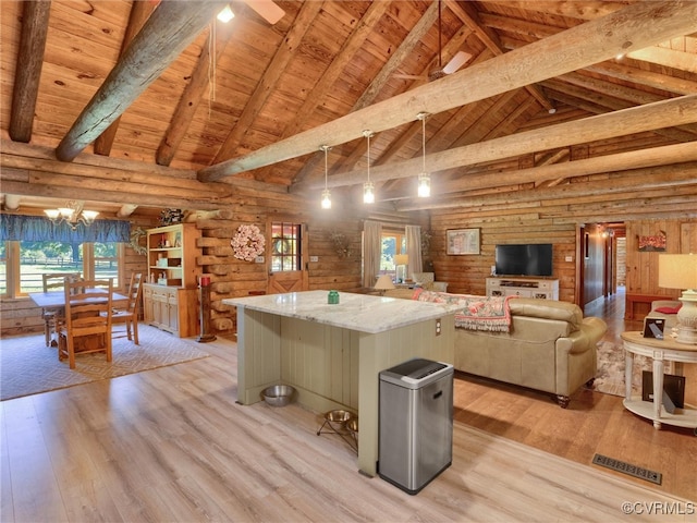 kitchen featuring light stone counters, a kitchen island, beamed ceiling, light wood-type flooring, and decorative light fixtures