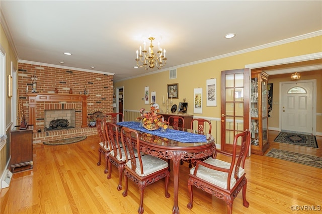 dining area featuring crown molding, light hardwood / wood-style flooring, a notable chandelier, and a brick fireplace