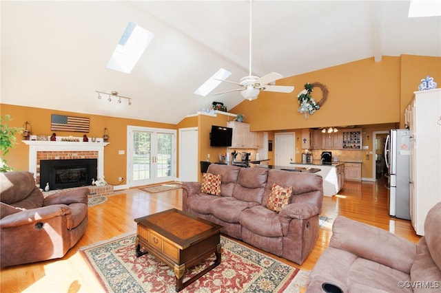 living room with a fireplace, high vaulted ceiling, a skylight, light hardwood / wood-style flooring, and ceiling fan