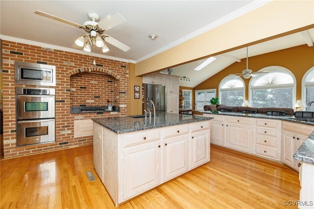 kitchen with lofted ceiling with skylight, a center island with sink, light hardwood / wood-style flooring, stainless steel appliances, and ceiling fan