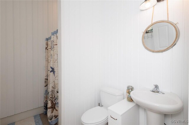 bathroom featuring wood walls, a shower with curtain, toilet, and sink