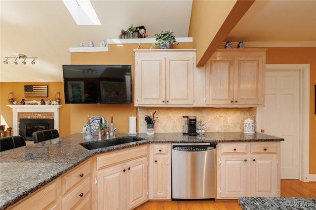 kitchen featuring dishwasher, lofted ceiling with skylight, dark stone counters, and a fireplace