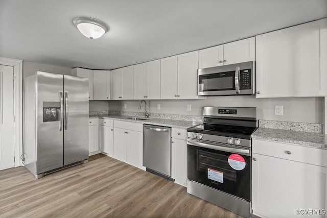 kitchen with stainless steel appliances, white cabinetry, sink, and light hardwood / wood-style flooring