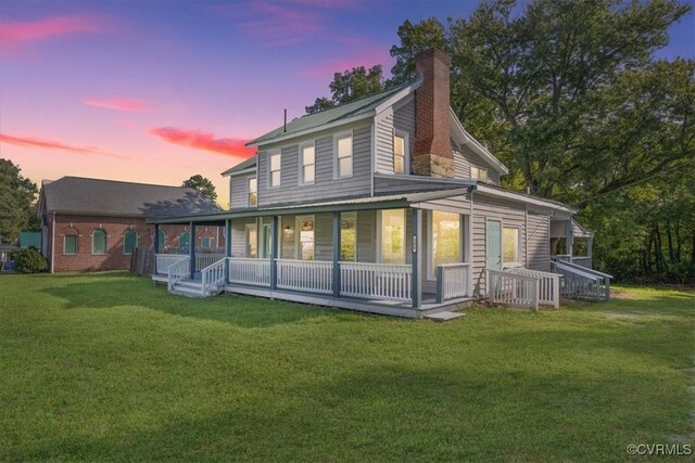 back house at dusk with a yard and covered porch