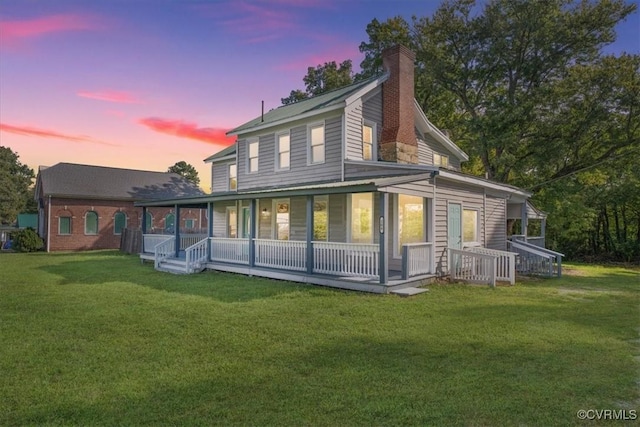 back house at dusk featuring a porch and a yard