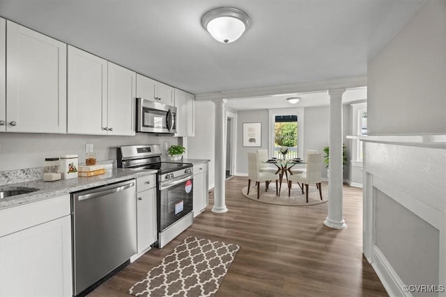 kitchen with ornate columns, white cabinetry, appliances with stainless steel finishes, and light stone countertops