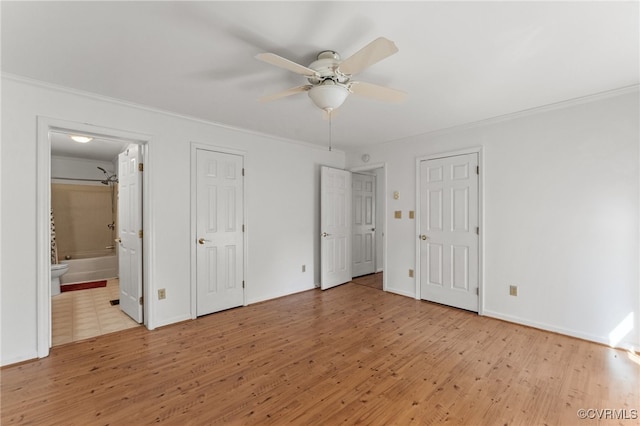 unfurnished bedroom featuring crown molding, light hardwood / wood-style flooring, connected bathroom, ceiling fan, and multiple closets