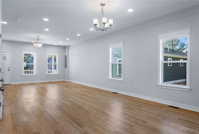 unfurnished room featuring plenty of natural light, ornamental molding, a notable chandelier, and light hardwood / wood-style flooring