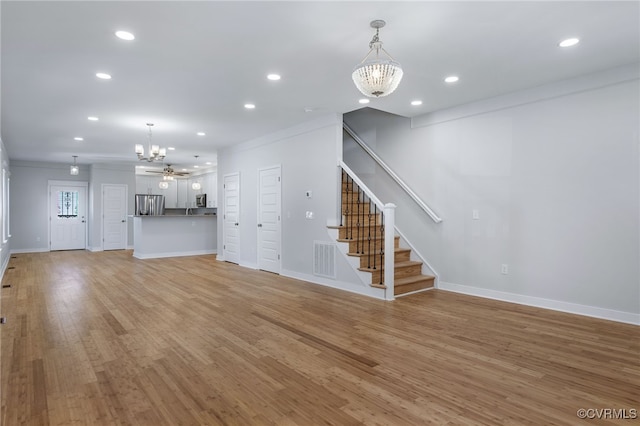 unfurnished living room featuring ceiling fan with notable chandelier, light wood-type flooring, and crown molding