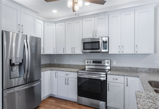 kitchen with white cabinetry, ceiling fan, light stone counters, appliances with stainless steel finishes, and light wood-type flooring