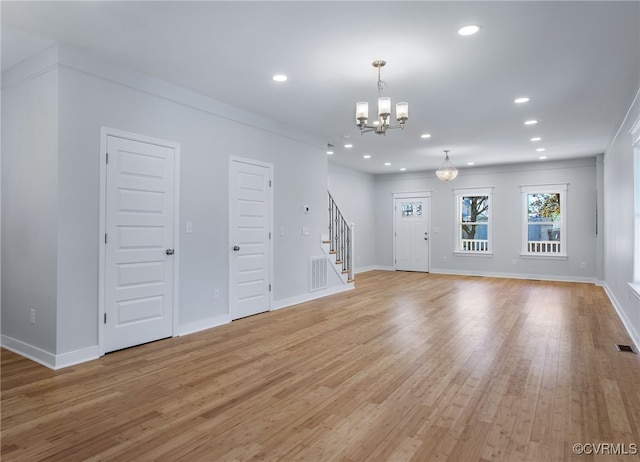 unfurnished living room with crown molding, an inviting chandelier, and light wood-type flooring