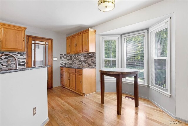 kitchen featuring light wood-type flooring, decorative backsplash, dark stone countertops, and a wealth of natural light