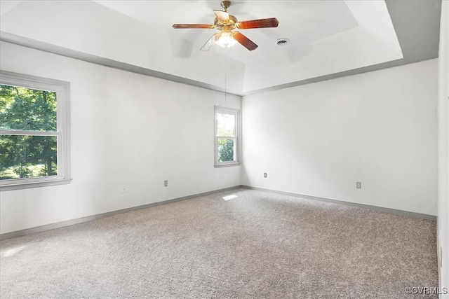 empty room featuring a tray ceiling, ceiling fan, and carpet flooring