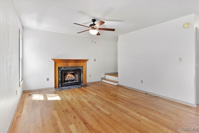 unfurnished living room featuring a high end fireplace, light wood-type flooring, and ceiling fan