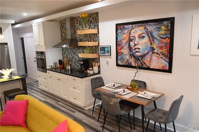 interior space featuring white cabinetry, appliances with stainless steel finishes, range hood, dark stone countertops, and dark hardwood / wood-style flooring