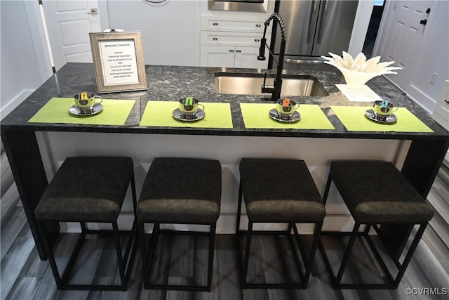 kitchen with white cabinets, a breakfast bar area, a center island with sink, and sink