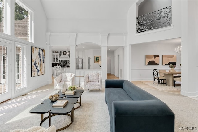 living room featuring a high ceiling, decorative columns, a chandelier, and light colored carpet