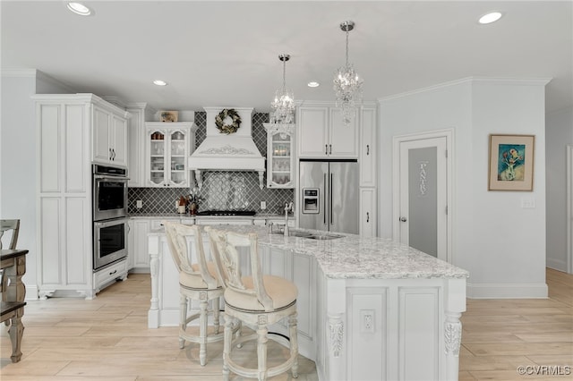 kitchen featuring premium range hood, a center island with sink, appliances with stainless steel finishes, and white cabinetry