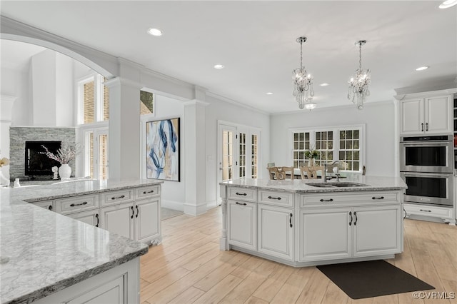 kitchen featuring an island with sink, white cabinets, stainless steel double oven, and a stone fireplace