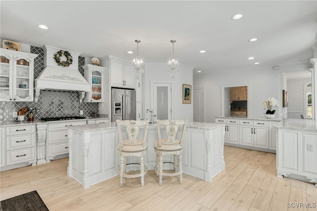 kitchen featuring high end refrigerator, white cabinetry, an island with sink, and decorative light fixtures