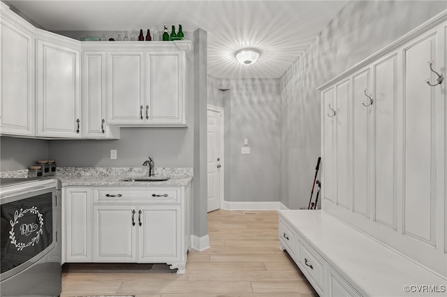 clothes washing area with cabinets, light hardwood / wood-style floors, and sink