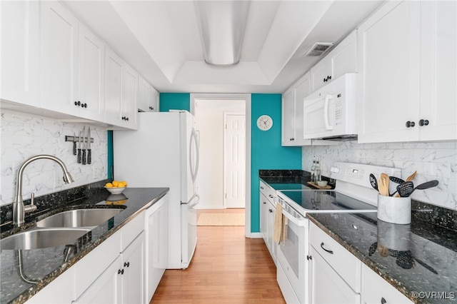 kitchen with sink, a raised ceiling, white appliances, dark stone counters, and white cabinets