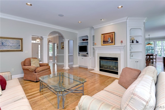 living room with light wood-type flooring, crown molding, a fireplace, and ornate columns