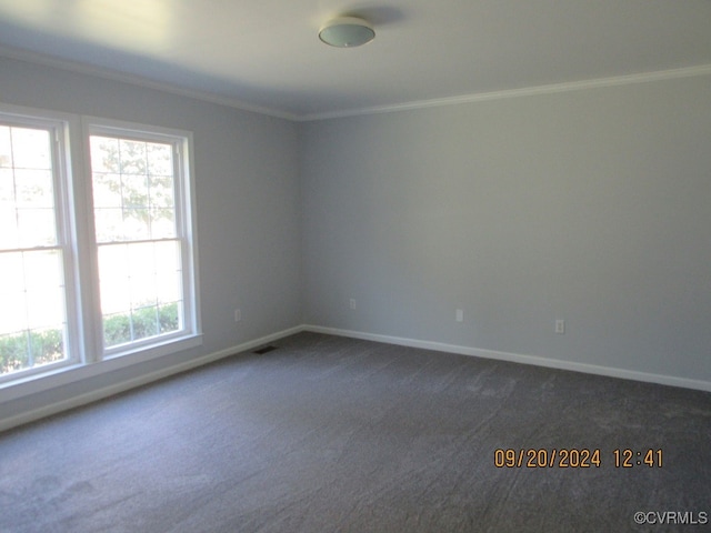 unfurnished room with ornamental molding, a wealth of natural light, and dark colored carpet