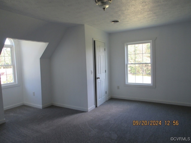 bonus room with dark colored carpet, vaulted ceiling, and a textured ceiling