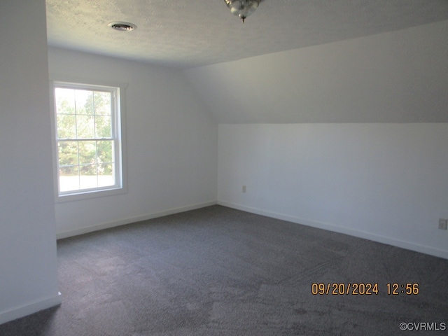 additional living space featuring a textured ceiling, vaulted ceiling, and dark carpet