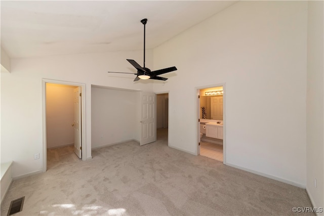 unfurnished bedroom with ceiling fan, high vaulted ceiling, ensuite bathroom, light carpet, and a closet