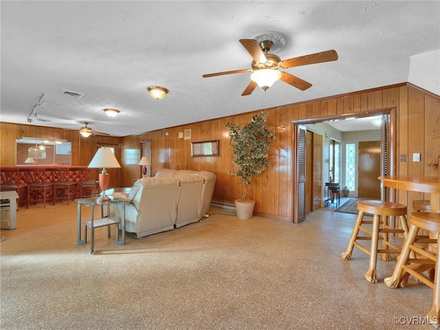 living room with ceiling fan, baseboard heating, and wood walls