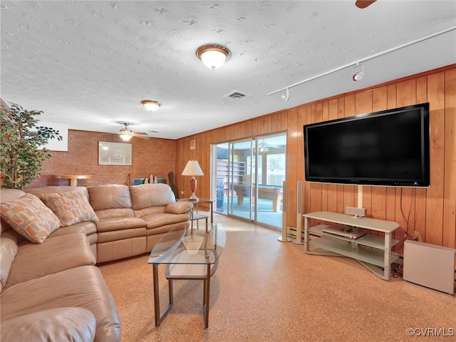 living room featuring ceiling fan, a textured ceiling, and wood walls